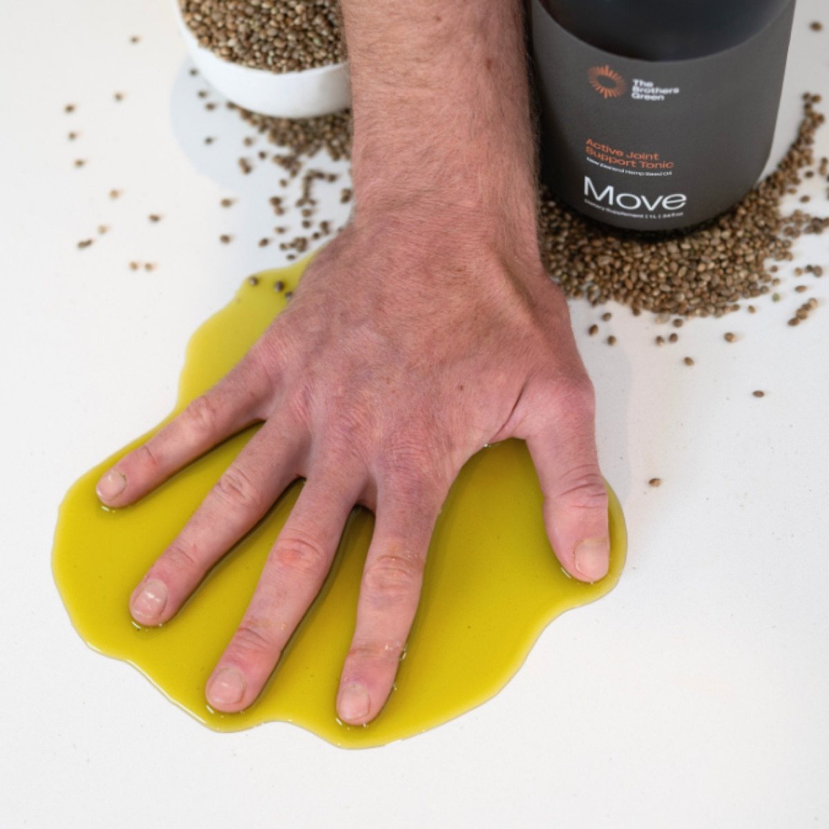 Hand pressed into a pool of golden hemp seed oil beside a bottle of Move