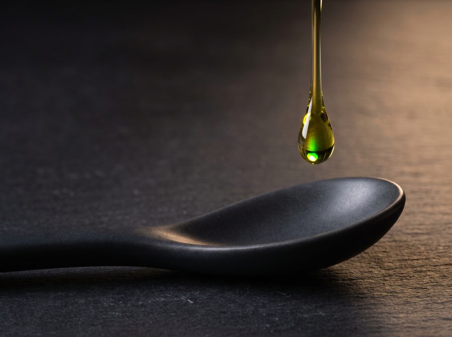 A drop of golden-green hemp oil falling toward a dark ceramic spoon