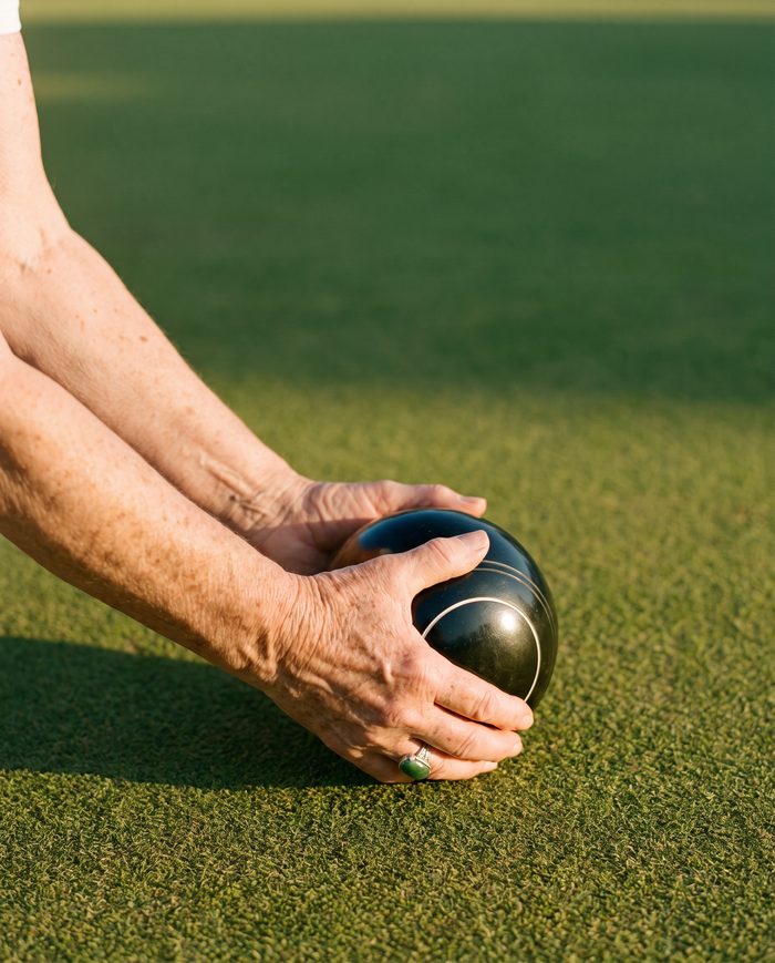 A hand steadying a bowls ball on the green at golden hour