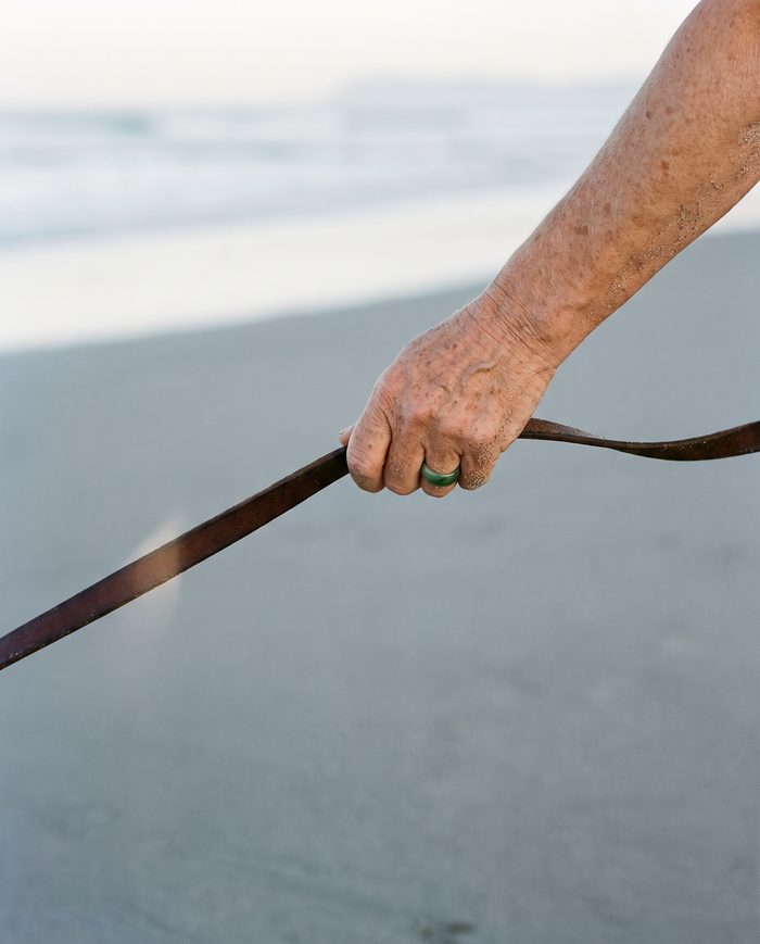 A hand holding a taut leather dog lead on wet sand
