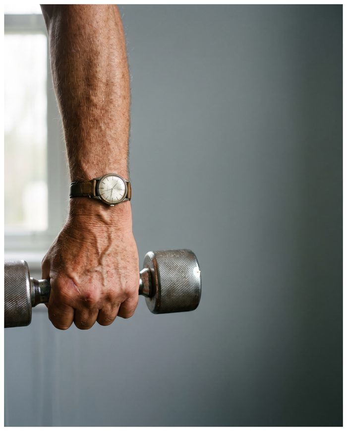 A hand lifting a steel dumbbell in soft window light